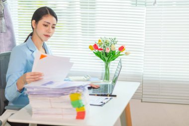 İş kadını masasında yığılmış çok sayıdaki yatırım belgelerini incelemek için belgeleri inceliyor. İş kadını masasında yığılmış çok sayıda belge bulmakta zorlanıyor..