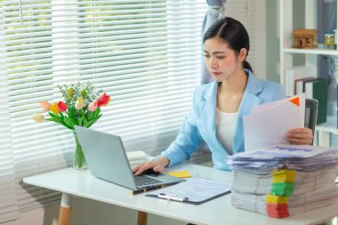 İş kadını, masasındaki çok sayıda belgenin hesaplarını kontrol etmek ve iş planını analiz etmek için belge arayışında olduğunu vurguladı. İş kadını çok sayıda belgenin altını çizdi