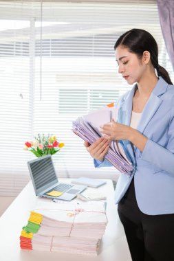 İş kadını masasında yığılmış çok sayıdaki yatırım belgelerini incelemek için belgeleri inceliyor. İş kadını masasında yığılmış çok sayıda belge bulmakta zorlanıyor..