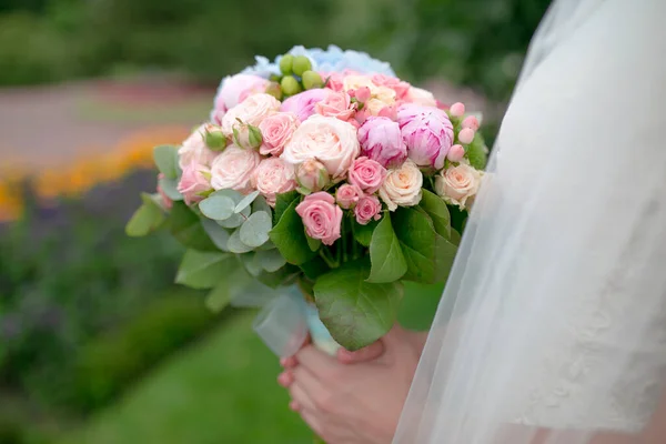 Bride holding wedding bouquet of peonies and roses in her hands. Modern bridal bouquet.