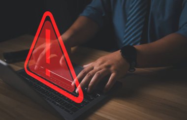 Üçgen uyarı işareti, kodlama, şifreleme, hacker, suç, virüs içeren dizüstü bilgisayar kullanan bir bilgisayar korsanı veya programcı. Kırmızı uyarı işareti olan bilgisayar.