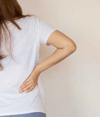 Sırt ağrısı yüzünden belini rahatsız eden genç bir kadın.