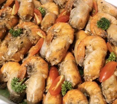 Taze otlar ve vişneli domateslerle süslenmiş lezzetli karides tabağının yakın görüntüsü.