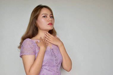 Asian young woman touching her neck by the hands due to neck pain. Concept of sore throat, pharyngitis, laryngitis, esophagitis, thyroiditis, lthyrotoxicosis, choking or dysphagia. clipart