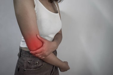 Beyaz atletli ve dirseğini tutan genç bir kadın. Ağrıyı göstermek için kırmızıyla işaretlenmiş..