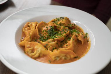 Gül soslu Ricotta ve ıspanaklı ravioli, soğanla süslenmiş, derin bir tabakta servis ediliyor.