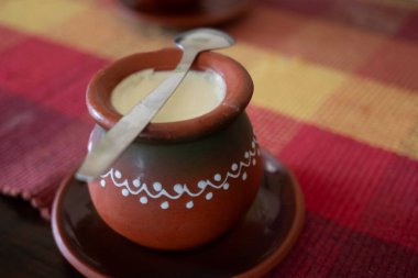 Sırp mutfağından popüler bir içecek olan ev yapımı mayalanmış süt, üzerinde kaşık bulunan geleneksel bir kil çaydanlıkta servis ediliyor.