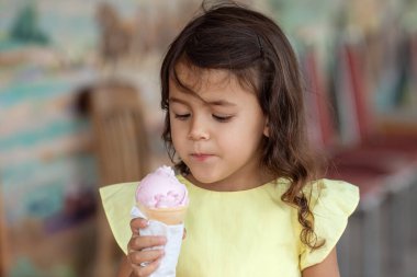 Yazlık elbiseli küçük kız kafeteryada sıcak bir günde dondurma yiyor, çocukluk anıları ve yaz tatili konsepti.