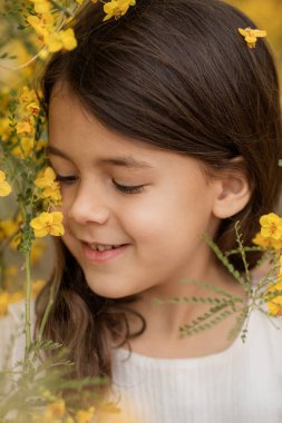 Kapanış baharı ya da yaz portresi. Çiçekleri açan, çocukluk anıları olan, gülümseyen küçük bir kız resmi.