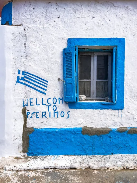 Welcome to Pserimos text in english language and national Greek flag painted on a white washed wall, blue window frame. Travel destination concept. Typical Greece style background with copy space.