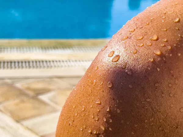 Water drops on sun kissed skin. Close-up on naked shoulder after swimming in pool. Summer travel and hotel resort background, copy space. Sun protection and skin care theme.
