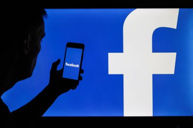 Vilnius, Litvanya - 6 Şubat 2022: Facebook ve Meta şirketi logosu akıllı telefon ve bilgisayar ekranlarında. Facebook uygulamasını elinde tutan adam silueti