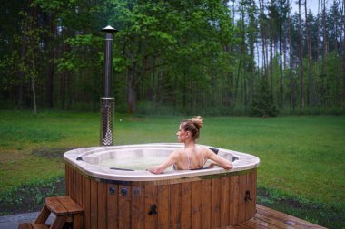 Genç ve mutlu bir kadın jakuzide dinleniyor. Ormanların dışındaki sağlık merkezinin tadını çıkarıyorum. Sıcak banyo spa merkezi. Yüksek kalite fotoğraf
