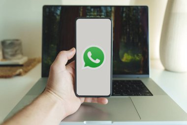 Londra, İngiltere - 19 Ekim 2024: Whatsapp chat uygulaması logosu cep telefonu ekranında. Whatsapp sohbet uygulamasını bilgisayarın arka planında akıllı telefondan tutan kişi