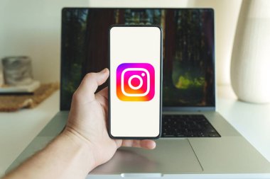 Londra, İngiltere - 19 Ekim 2024: Cep telefonu ekranında Instagram uygulama logosu. Bilgisayarın arka planında akıllı telefonda Instagram uygulaması tutan kişi