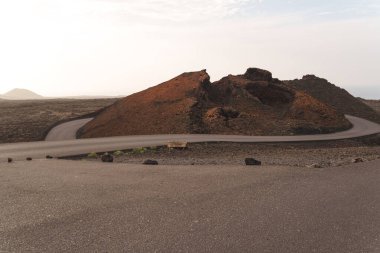Lanzarote 'de volkanik bir manzara, kırmızı kum, lav kayaları ve sisli bir gökyüzünün altındaki dağlar. Yüksek kalite fotoğraf
