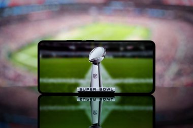 Arka planda bulanık bir Amerikan futbol stadyumuyla Super Bowl kupasını gösteren bir akıllı telefon. 13 Ocak 2025