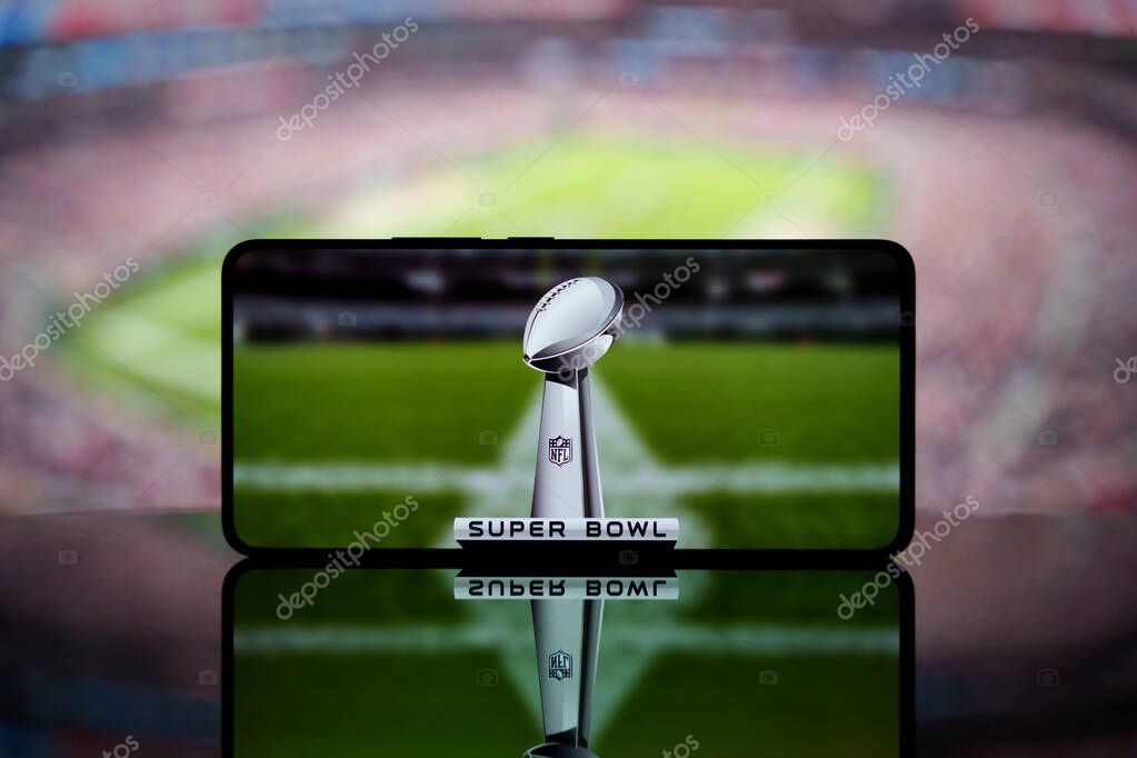 A smartphone displaying the Super Bowl trophy with a blurred American football stadium in the background. January 13, 2025
