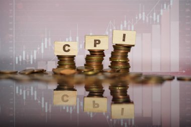 Arkaplanda borsa grafiği olan ve Tüketici Fiyat Endeksi 'ni ve enflasyon ve ekonomi üzerindeki etkisini temsil eden bozuk para yığınlarının üzerine istiflenmiş tahta bloklar...