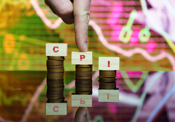 Wooden blocks spelling CPI stacked on piles of coins with a stock market graph in the background, representing the Consumer Price Index and its impact on inflation and the economy..