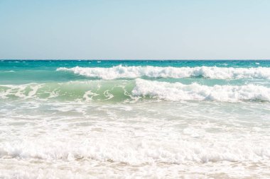  Okyanus dalgaları açık, açık mavi bir gökyüzünün altında kumlu bir kıyıya yuvarlanıyor. Yüksek kalite fotoğraf