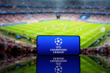 Arka planda bulanık bir futbol stadyumu bulunan UEFA Şampiyonlar Ligi logosunu gösteren akıllı telefon. Avrupa futbol yarışması ve spor etkinliği konsepti. 17 Mart 2025