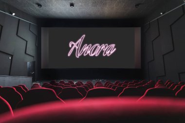 Sinema ekranında Anora, neon senaryoda Oscar ödüllü bir film olarak gösteriliyor. Boş kırmızı koltuklar tiyatroyu doldurur. Yüksek kalite fotoğraf. 5 Nisan 2025
