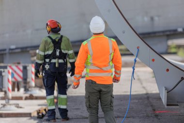 Güvenlik teçhizatlı iki inşaat işçisi endüstriyel bir şantiyedeki büyük metal yapıyı izliyor. Yüksek kalite fotoğraf