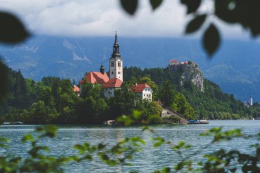 Bled Gölü 'ndeki İkonik Varsayım Kilisesi, ağaçların arasına kurulmuş ve yeşil ağaç yapraklarıyla çerçevelenmiş. Yüksek kalite fotoğraf