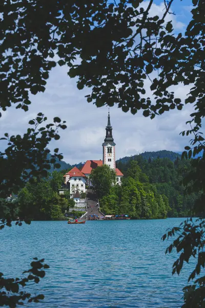 Bled Gölü 'ndeki İkonik Varsayım Kilisesi, ağaçların arasına kurulmuş ve yeşil ağaç yapraklarıyla çerçevelenmiş. Yüksek kalite fotoğraf