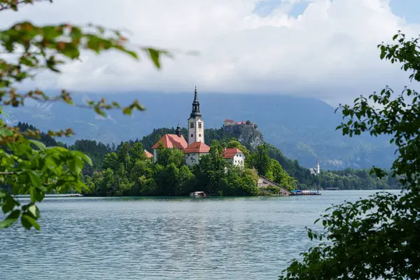 Bled Gölü 'ndeki İkonik Varsayım Kilisesi, ağaçların arasına kurulmuş ve yeşil ağaç yapraklarıyla çerçevelenmiş. Yüksek kalite fotoğraf