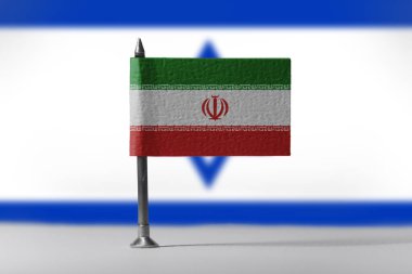 Arka planda bulanık İsrail bayrağı bulunan küçük İran bayrağı, İran ile İsrail arasındaki siyasi çatışmayı veya diplomatik gerginliği simgeliyor. Yüksek kalite fotoğraf