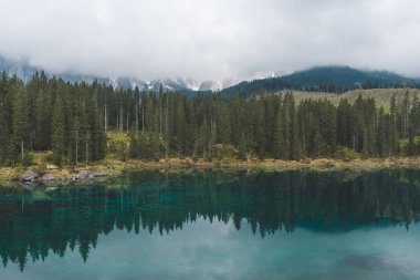Dolomites, İtalya 'daki Carezza Gölü' nün arka planında turkuaz su, çam ormanı ve sisli dağlar bulunur. Yüksek kalite fotoğraf