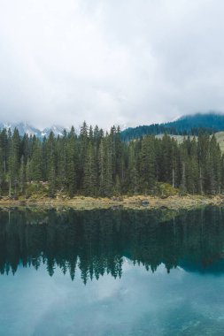 Dolomites, İtalya 'daki Carezza Gölü' nde, çam ormanı ve bulutlu dağ manzarasını yansıtan turkuaz su ile. Yüksek kalite fotoğraf