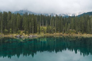 Dolomites, İtalya 'daki Carezza Gölü' nde, çam ormanı ve bulutlu dağ manzarasını yansıtan turkuaz su ile. Yüksek kalite fotoğraf