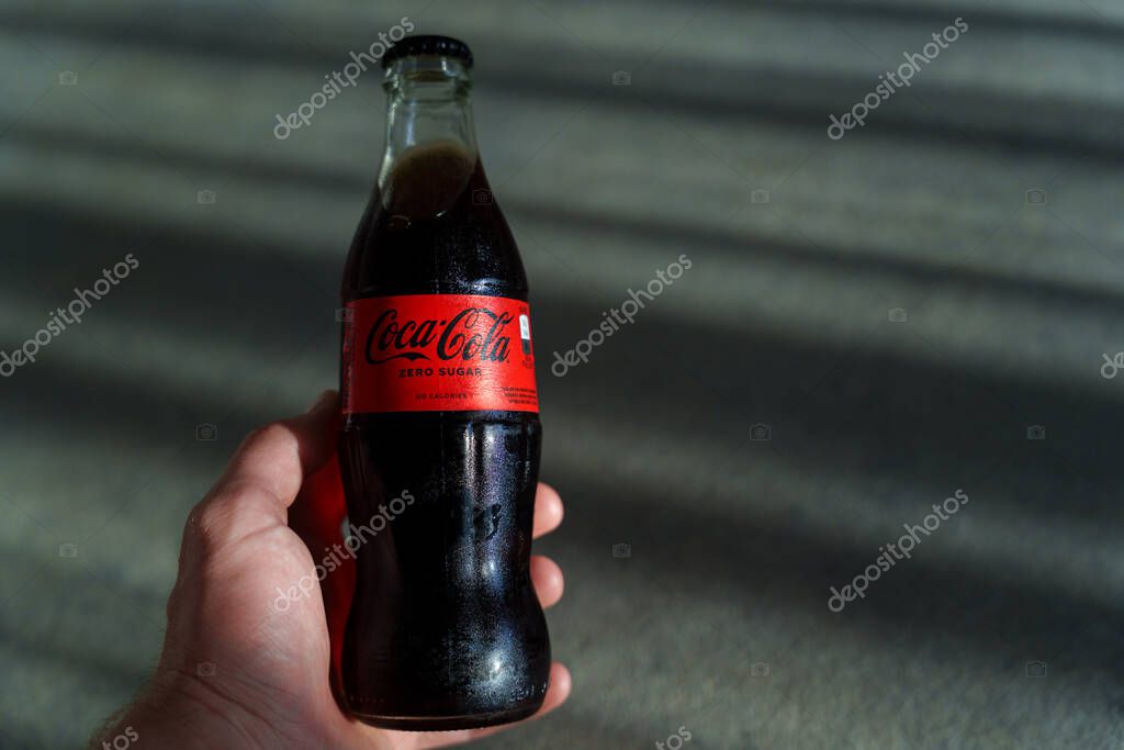 Hand holding a chilled glass Coca-Cola Zero Sugar bottle with condensation and red label. High quality photo