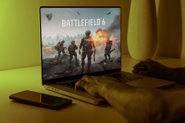  Battlefield 6 oyun ekranını gösteren bir dizüstü bilgisayar. Bir oyuncu sıcak oda ışığında klavyeyi kullanır. Yüksek kalite fotoğraf
