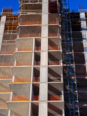 Portakal rengi güvenlik bariyerleri ve açık mavi gökyüzü olan modern beton bir binanın dikey görüntüsü. Yüksek kalite fotoğraf