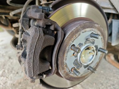 Close-up of a disassembled car wheel showing the brake caliper, used brake rotor, and wheel hub with studs, ready for repair or maintenance. High quality photo
