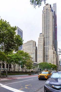 Manhattan, New York 'taki 5. Cadde manzarası. Yüksek gökdelenler, ağaçlar ve klasik sarı taksi. Turizm, seyahat, alışveriş, iş, yaşam tarzı ve ikonik NYC simgelerini temsil eder