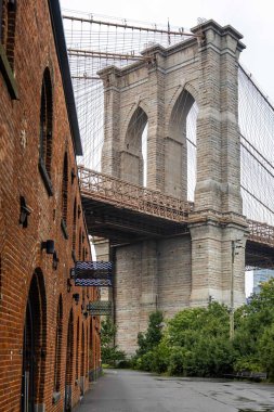 Doğu Nehri boyunca uzanan ikonik Brooklyn Köprüsü. Arka planda Manhattan silueti ve oradan geçen bir tekne var. Seyahat, turizm, mimari ve New York Şehri yaşam tarzı temaları için mükemmel.