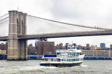 Doğu Nehri boyunca uzanan ikonik Brooklyn Köprüsü. Arka planda Manhattan silueti ve oradan geçen bir tekne var. Seyahat, turizm, mimari ve New York Şehri yaşam tarzı temaları için mükemmel.