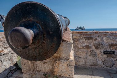 Petrovac, Montenegro, August 11, 2024. Kastio castle cannon in front of the Small Orthodox Church on the Island of Nedjelja Sveta clipart