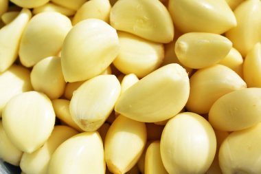 Taze soyulmuş sarımsaklı eldivenler güneşli ve parlak arka planda.