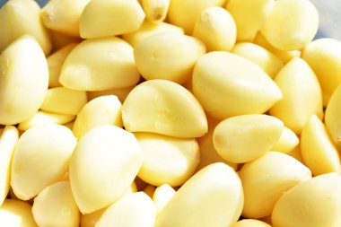 Taze soyulmuş sarımsaklı eldivenler güneşli ve parlak arka planda.