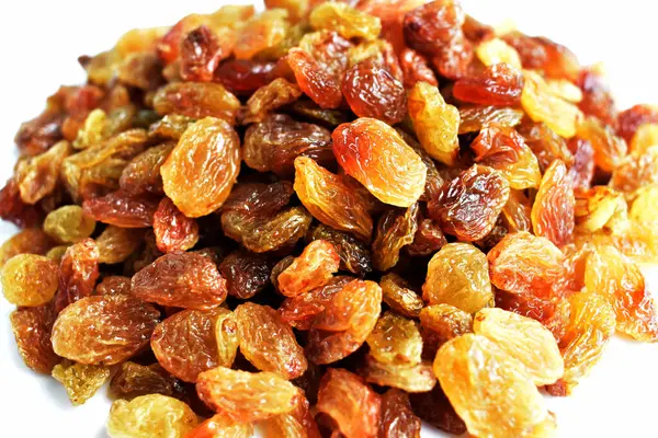 Beyaz arka planda izole edilmiş sarı ve kahverengi kuru üzüm yığınları. Güneşli ve parlak.