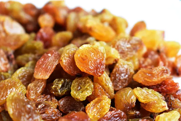 Beyaz arka planda izole edilmiş sarı ve kahverengi kuru üzüm yığınları. Güneşli ve parlak.