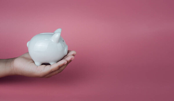 Hand holding a white piggy bank on a pink background. Savings and investment concepts.