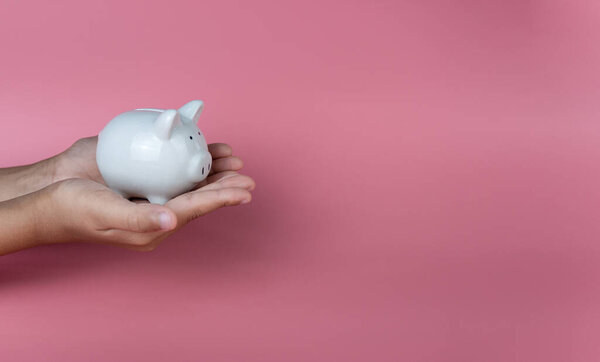 Hand holding a white piggy bank on a pink background. Savings and investment concepts.