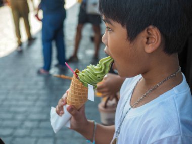 A boy wearing a white shirt is eating ice cream.